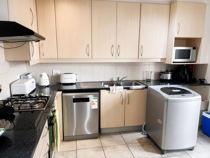 Functional kitchen featuring light wood cabinetry, granite countertops, gas hob, extractor fan, and built-in microwave with tiled flooring and backsplash.