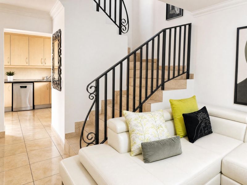 Open plan living area featuring a tiled staircase with decorative wrought iron railing, leading to a view of the adjacent kitchen with light wood cabinetry.