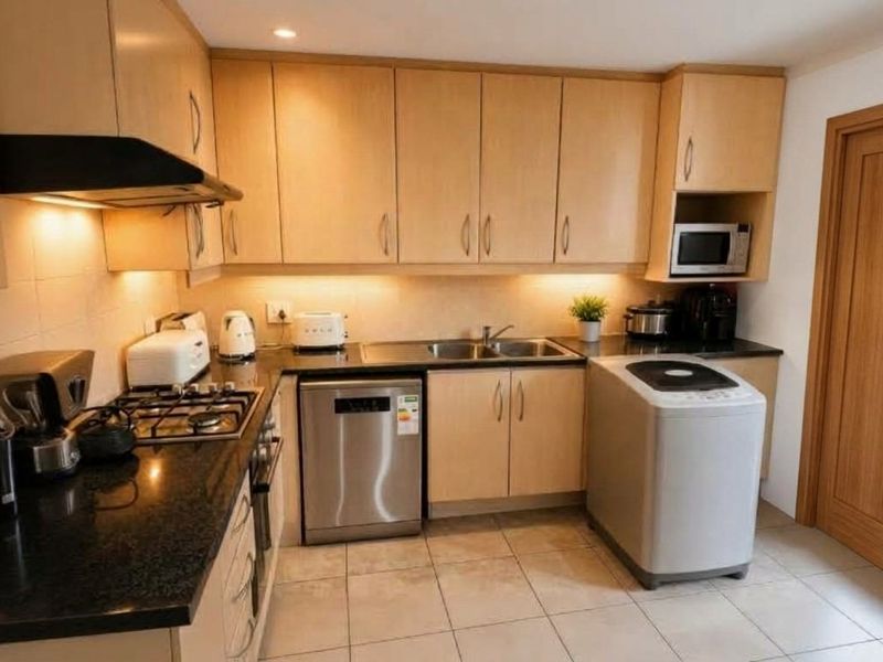 A functional kitchen featuring light wood cabinetry, granite countertops, a gas hob, extractor fan, and integrated microwave with tiled flooring.
