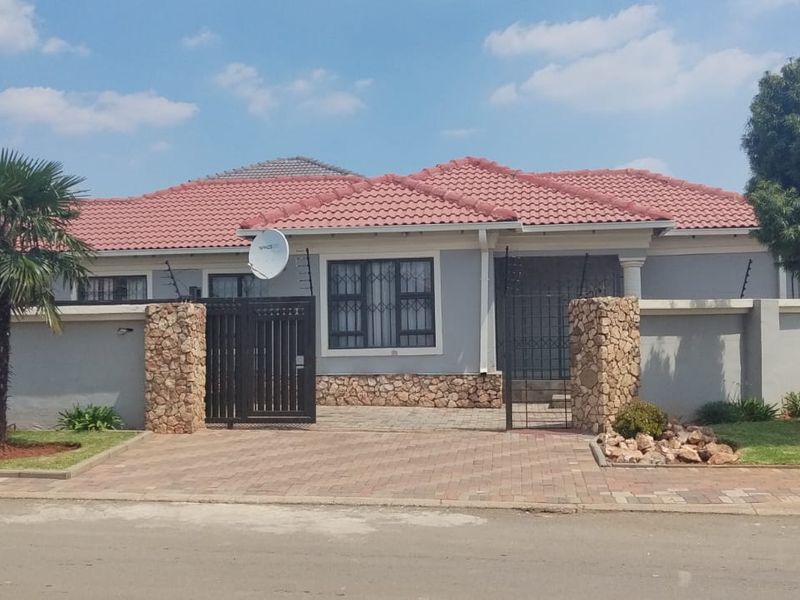 Front elevation of a single-story house featuring a tiled roof, stone-clad entrance pillars, paved driveway, and secure perimeter wall with electric fencing.