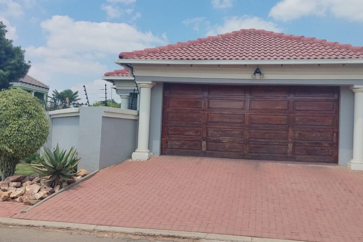 Front exterior view of a residential property featuring a paved driveway, double garage with wooden door, and perimeter walling with electric fencing.