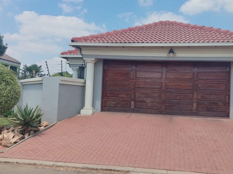 Front exterior view of a residential property featuring a paved driveway, double garage with wooden door, and perimeter walling with electric fencing.