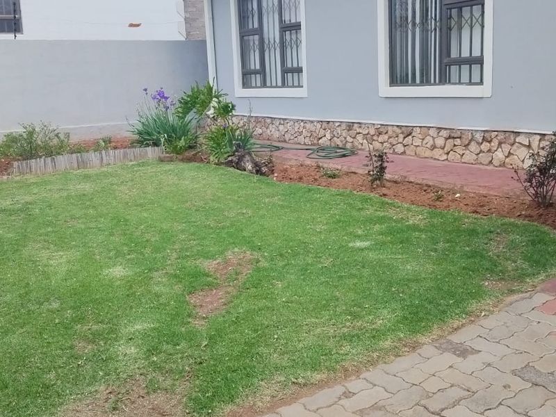 A rear garden area featuring a lawn, stone-clad exterior wall, security bars on windows, and paved access path.
