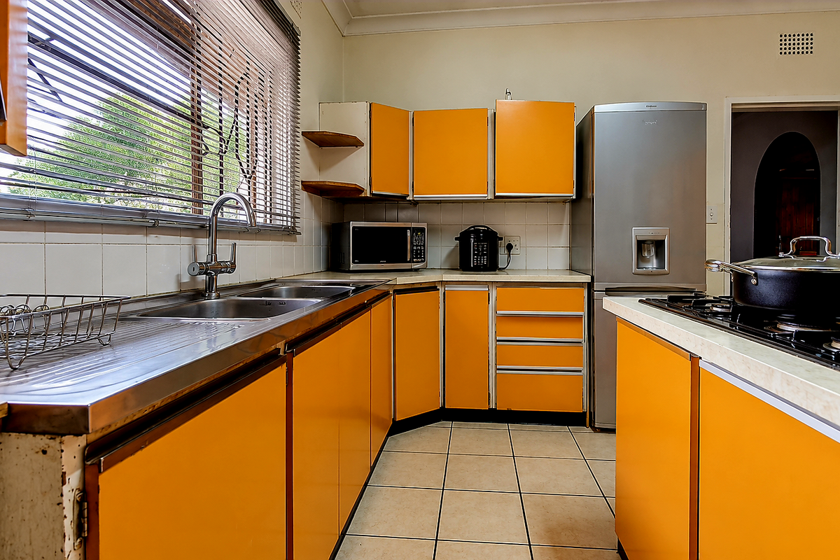 A functional kitchen featuring bright orange cabinetry, a stainless steel sink, and a gas hob, offering a dated aesthetic ready for modernization.