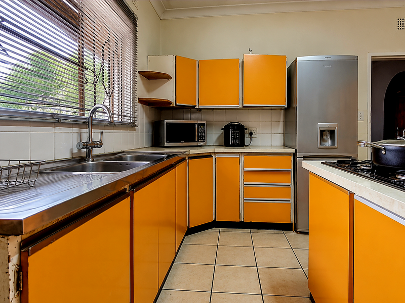 A functional kitchen featuring bright orange cabinetry, a stainless steel sink, and a gas hob, offering a dated aesthetic ready for modernization.