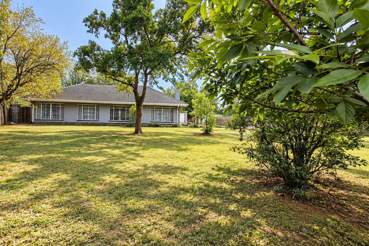A spacious rear garden featuring a well-maintained lawn, mature trees, and a view of the rear elevation of the house with a tiled roof.