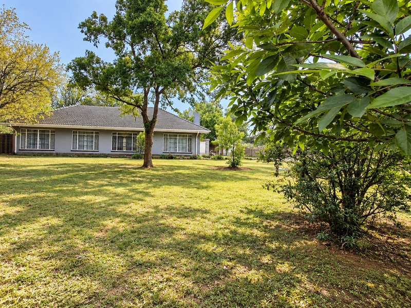 A spacious rear garden featuring a well-maintained lawn, mature trees, and a view of the rear elevation of the house with a tiled roof.