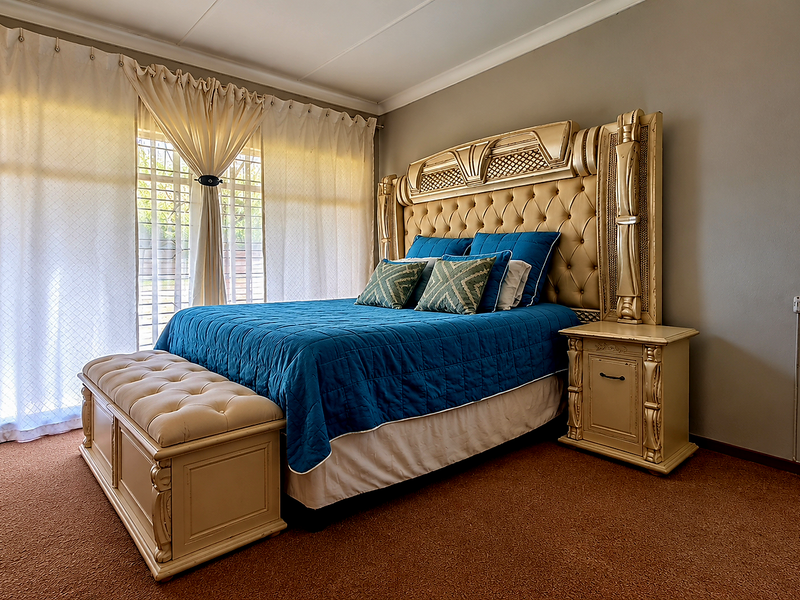 A spacious bedroom featuring carpeted flooring and a large sliding glass door with security gate, providing natural light and access to the exterior.