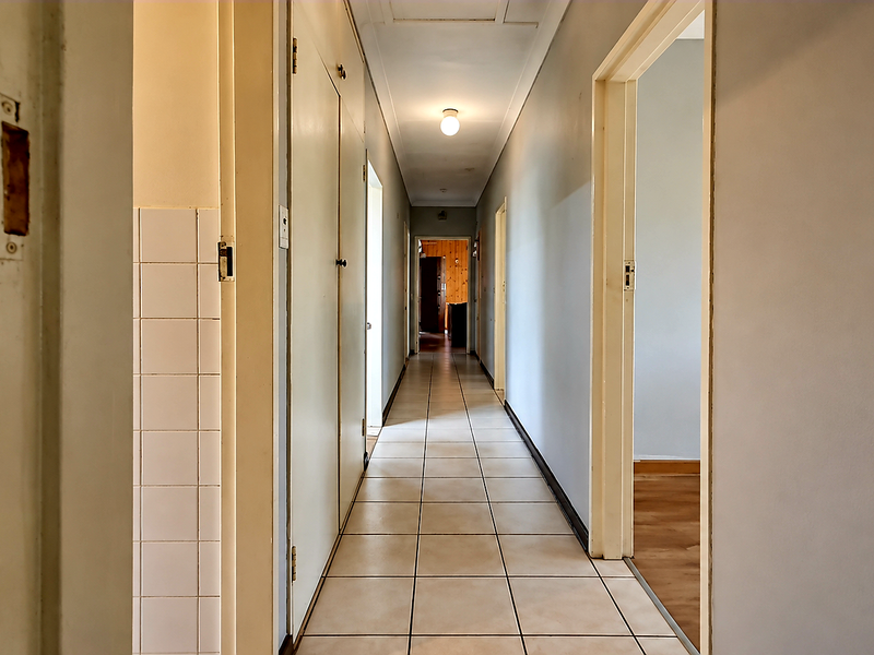 A long, tiled hallway featuring built-in storage cupboards and access to multiple rooms, providing a functional transition space within the home.