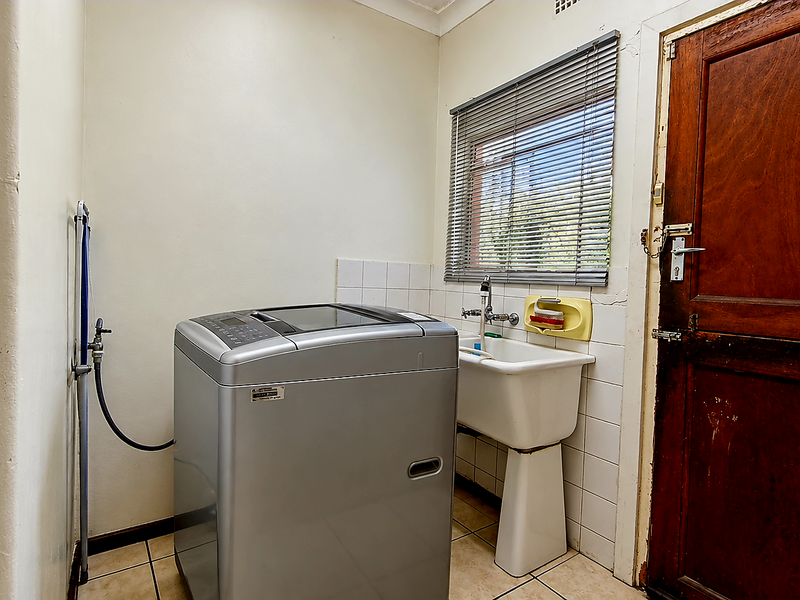 Functional laundry room featuring a pedestal sink, tiled splashback, and direct exterior access through a timber door.