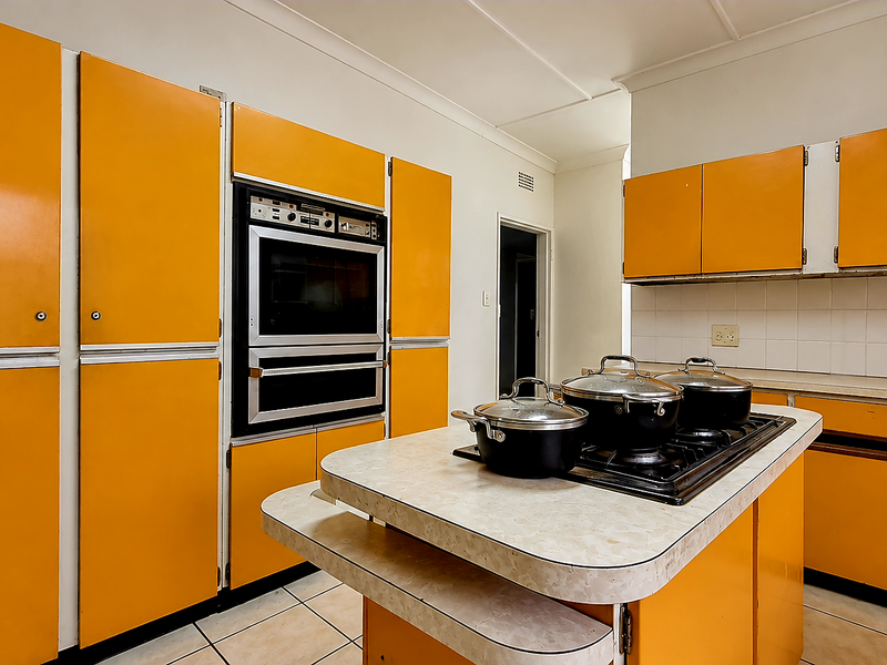 A dated kitchen featuring bright orange cabinetry, a built-in double oven, a central island with a cooktop, and tiled flooring.