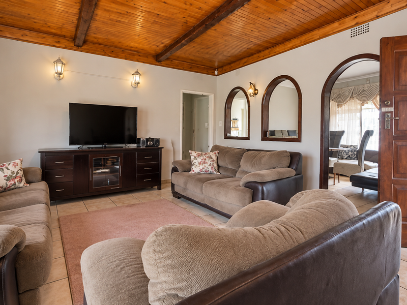 Spacious living room featuring a vaulted timber-clad ceiling with exposed beams, tiled flooring, and distinctive arched wall niches leading to an adjacent room.