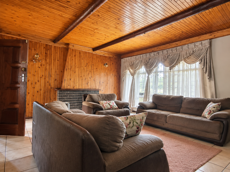 A living room featuring extensive timber-clad walls and ceiling, a brick fireplace, and tiled flooring, offering a traditional aesthetic with potential for modernization.