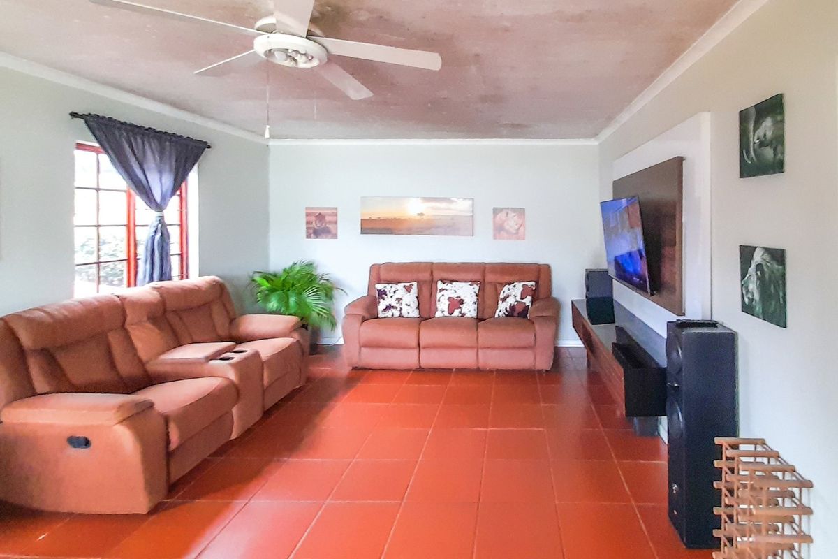 Spacious living room featuring terracotta tiled flooring, a ceiling fan, and a built-in media wall unit. The ceiling shows signs of staining.
