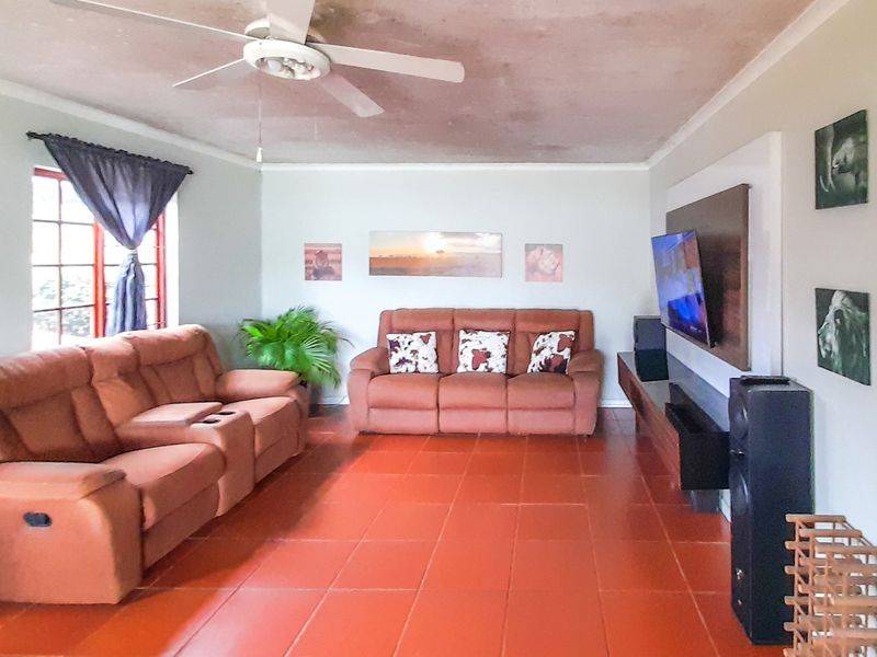 Spacious living room featuring terracotta tiled flooring, a ceiling fan, and a built-in media wall unit. The ceiling shows signs of staining.