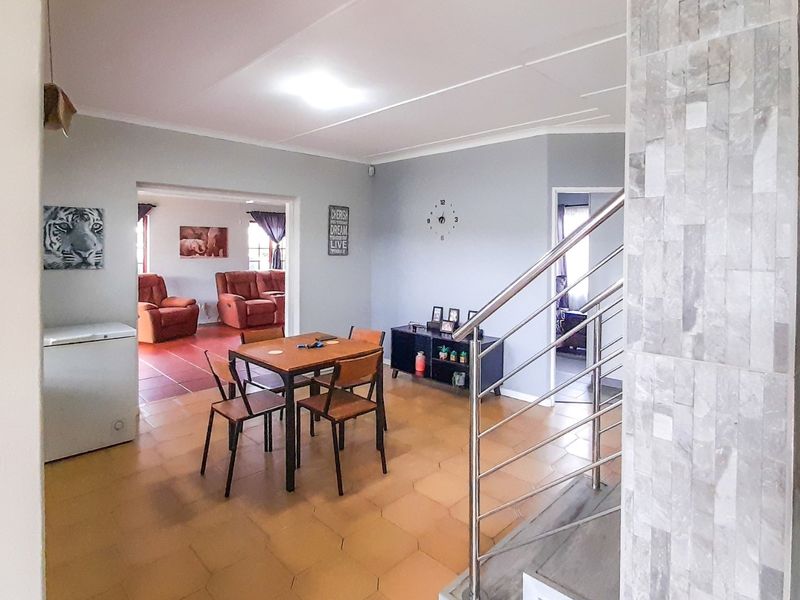 Open plan living area featuring tiled flooring, a stone-clad feature wall, and a modern stainless steel staircase railing leading to the upper level.