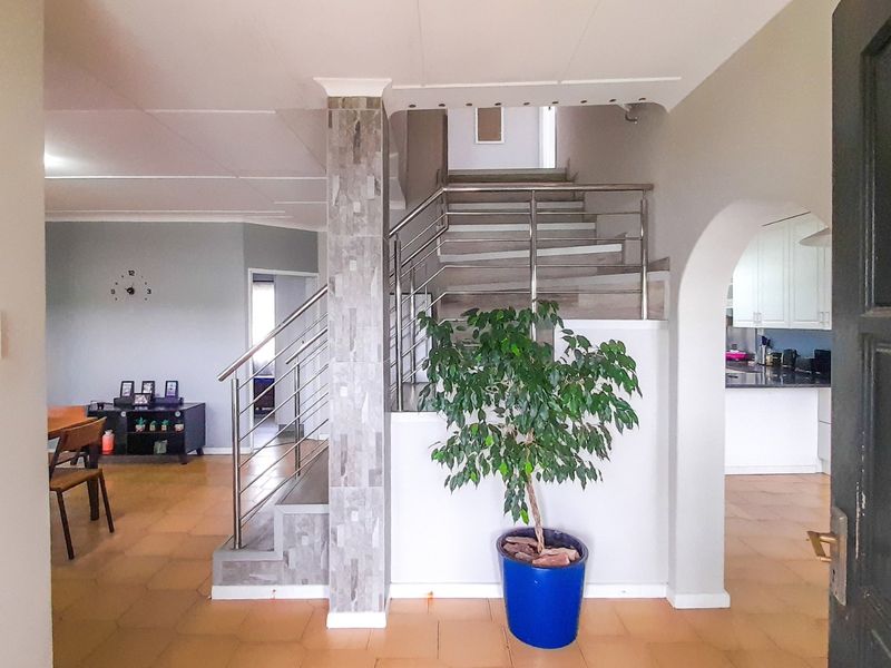 Welcoming entrance hall featuring a modern stainless steel staircase railing, stone-clad pillar, and tiled flooring, leading into the open-plan living and kitchen areas.