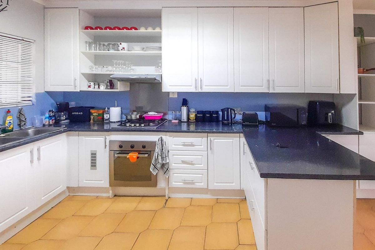 A functional kitchen featuring white shaker-style cabinetry, dark granite countertops, a gas hob, and an integrated oven with open shelving for storage.