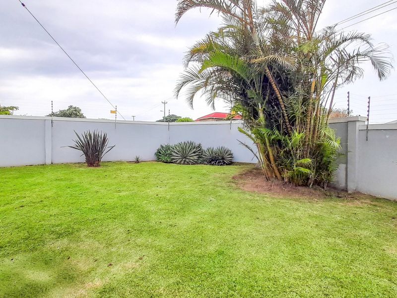 A well-maintained private garden featuring a lush lawn, established palm trees, and secure perimeter walling with electric fencing.