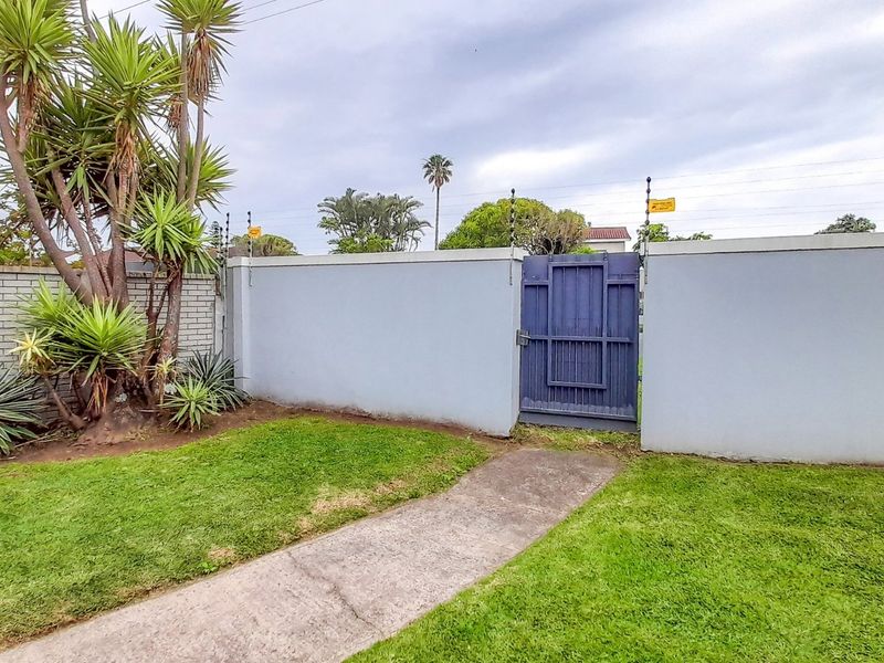 A secure rear garden area featuring a concrete pathway, perimeter walling with integrated electric fencing, and a private pedestrian access gate.