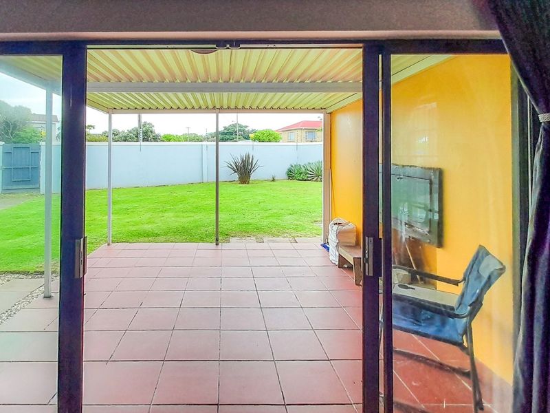 A covered patio area featuring tiled flooring and a built-in braai, overlooking a private garden with a boundary wall.