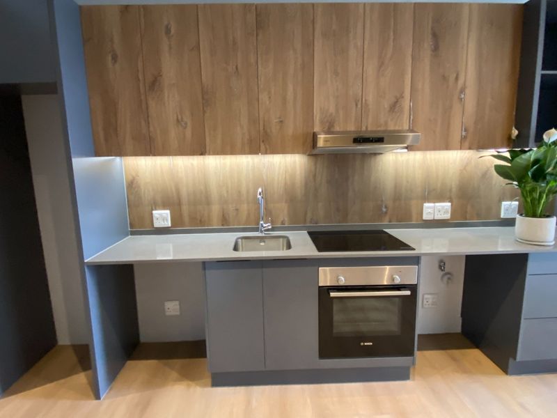 Modern kitchen featuring sleek grey cabinetry, wood-grain upper cabinets, stone countertops, and integrated stainless steel appliances including an oven and extractor fan.