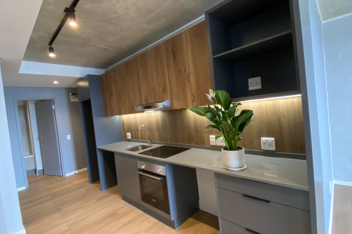 Modern kitchen featuring sleek grey and wood-tone cabinetry, quartz countertops, built-in appliances, and an industrial-style exposed concrete ceiling with track lighting.