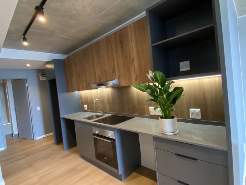 Modern kitchen featuring sleek grey and wood-tone cabinetry, quartz countertops, built-in appliances, and an industrial-style exposed concrete ceiling with track lighting.