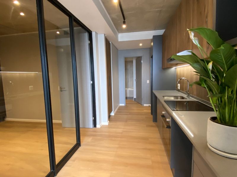 Modern kitchen featuring sleek cabinetry, stone countertops, integrated appliances, and an exposed concrete ceiling, adjacent to a glass-partitioned room.