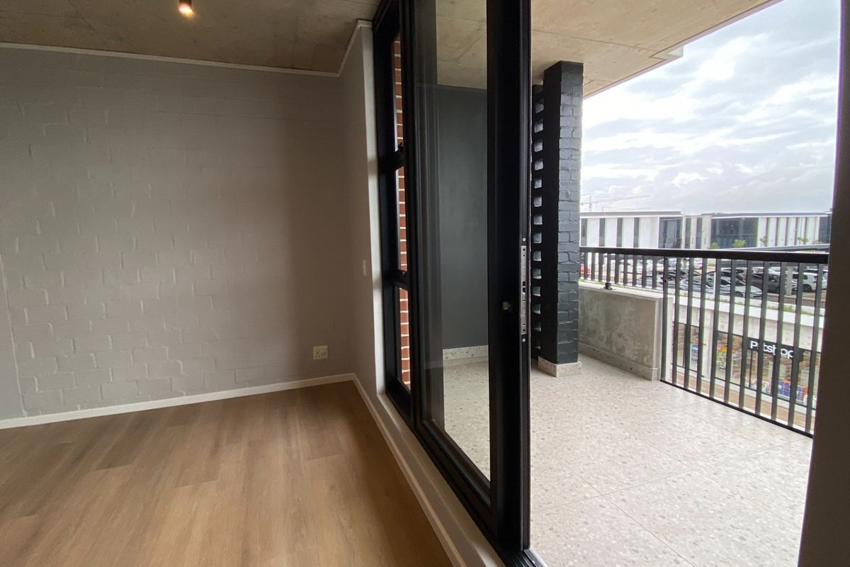 Modern open-plan living area featuring exposed concrete ceilings, laminate flooring, and seamless access to a private balcony through large sliding glass doors.