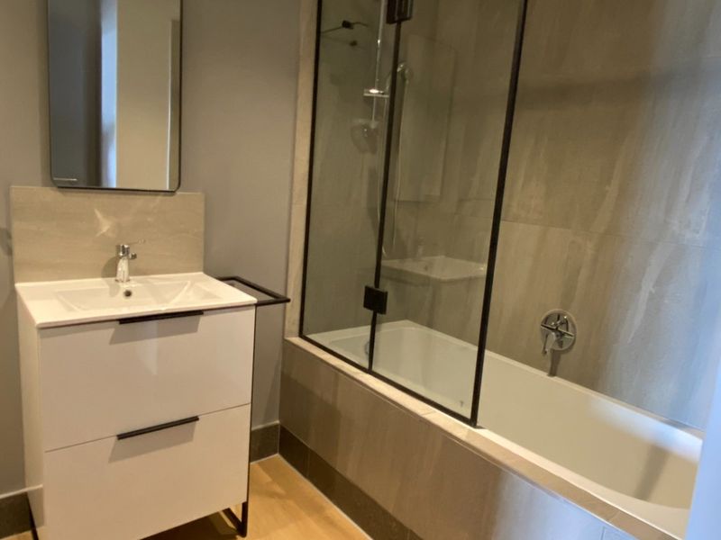Modern bathroom featuring a sleek vanity cabinet, a bathtub with a glass shower screen, and contemporary neutral tiling.