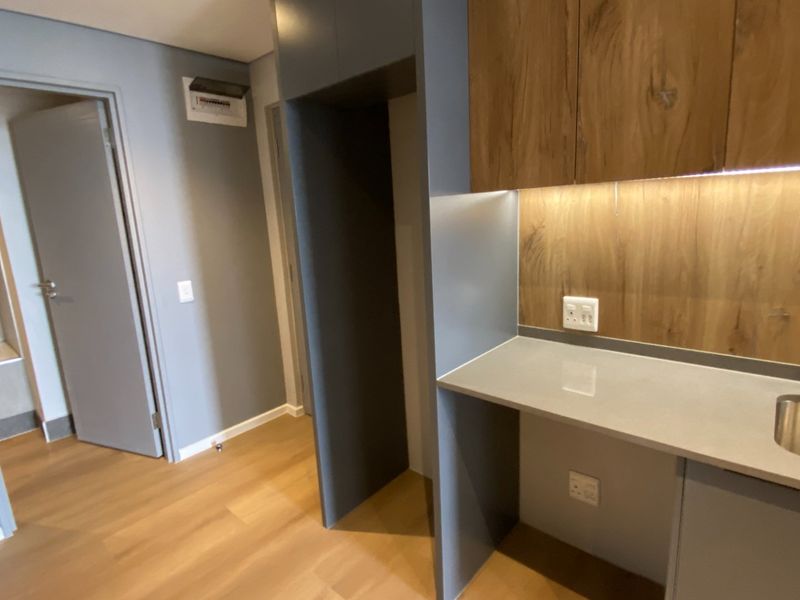 Modern kitchen area featuring sleek grey cabinetry, wood-look backsplash, stone countertops, and an integrated sink with contemporary fixtures.