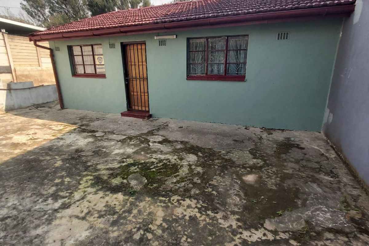 Rear exterior view of the property featuring a tiled roof, security gate, and a large concrete paved area showing significant weathering and staining.