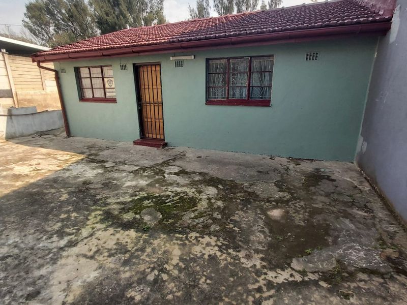 Rear exterior view of the property featuring a tiled roof, security gate, and a large concrete paved area showing significant weathering and staining.