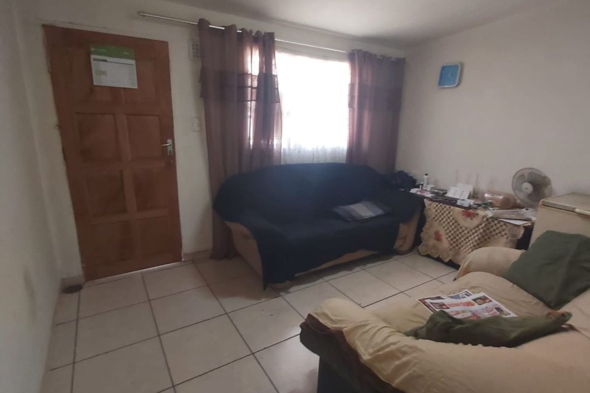 A living room featuring tiled flooring, a wooden entrance door, and a window with curtains, providing a basic functional living space.