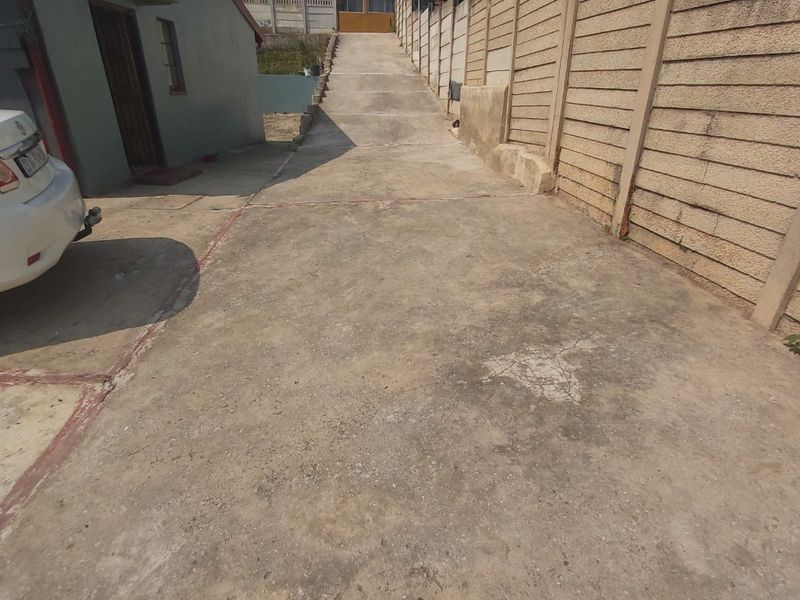 A concrete driveway leading up to the property, bordered by a precast concrete boundary wall.