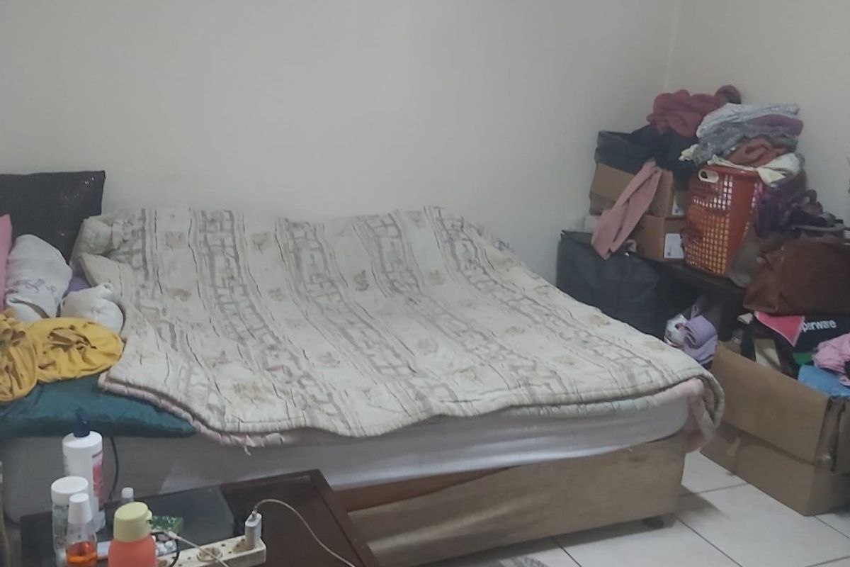 A bedroom featuring tiled flooring, currently cluttered with personal belongings and storage items.