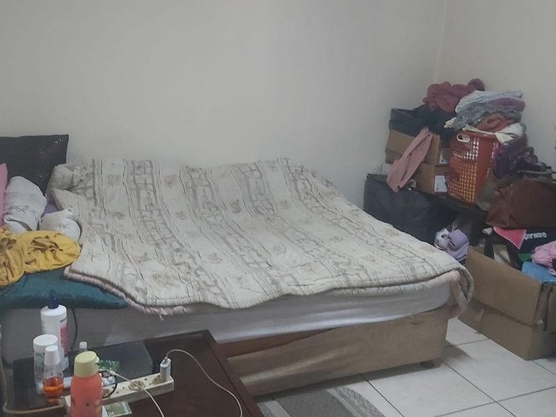 A bedroom featuring tiled flooring, currently cluttered with personal belongings and storage items.