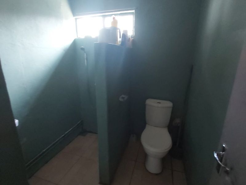 A functional bathroom featuring a toilet and a shower area separated by a partition wall, with tiled flooring and a small window.
