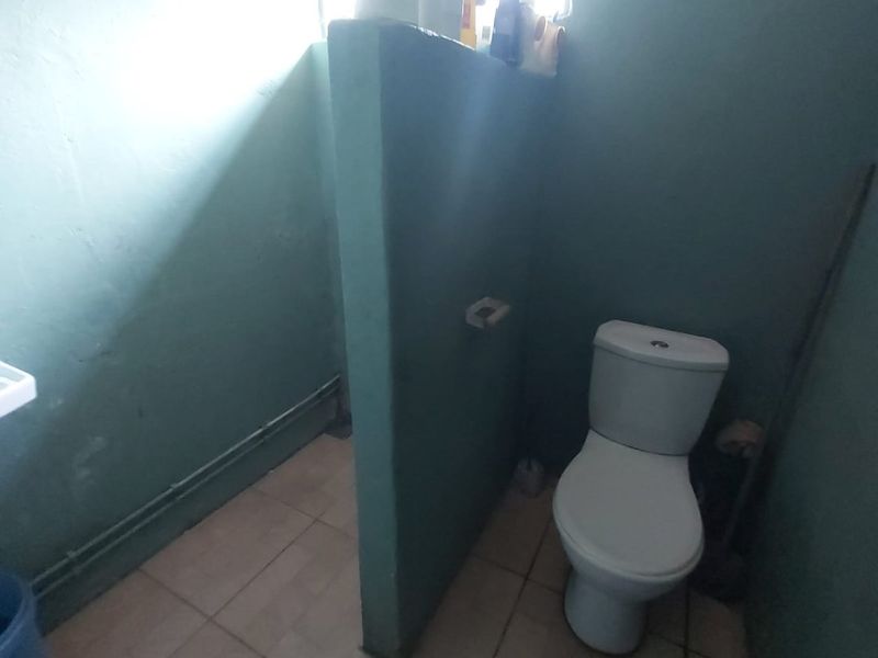 A small bathroom featuring a toilet and a partition wall, with tiled flooring and visible surface-mounted plumbing.