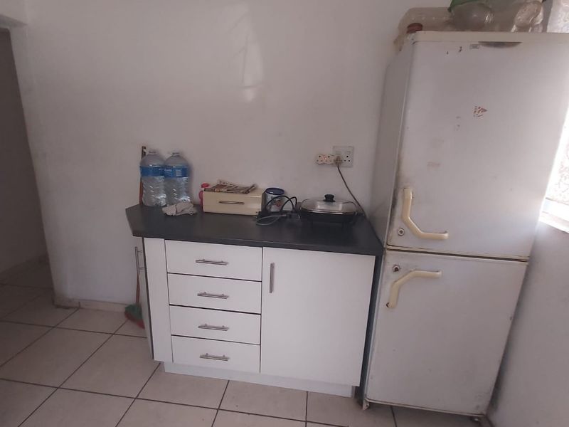 A compact kitchen area featuring basic cabinetry, laminate countertops, and tiled flooring, requiring cosmetic updates to improve its overall aesthetic and functionality.