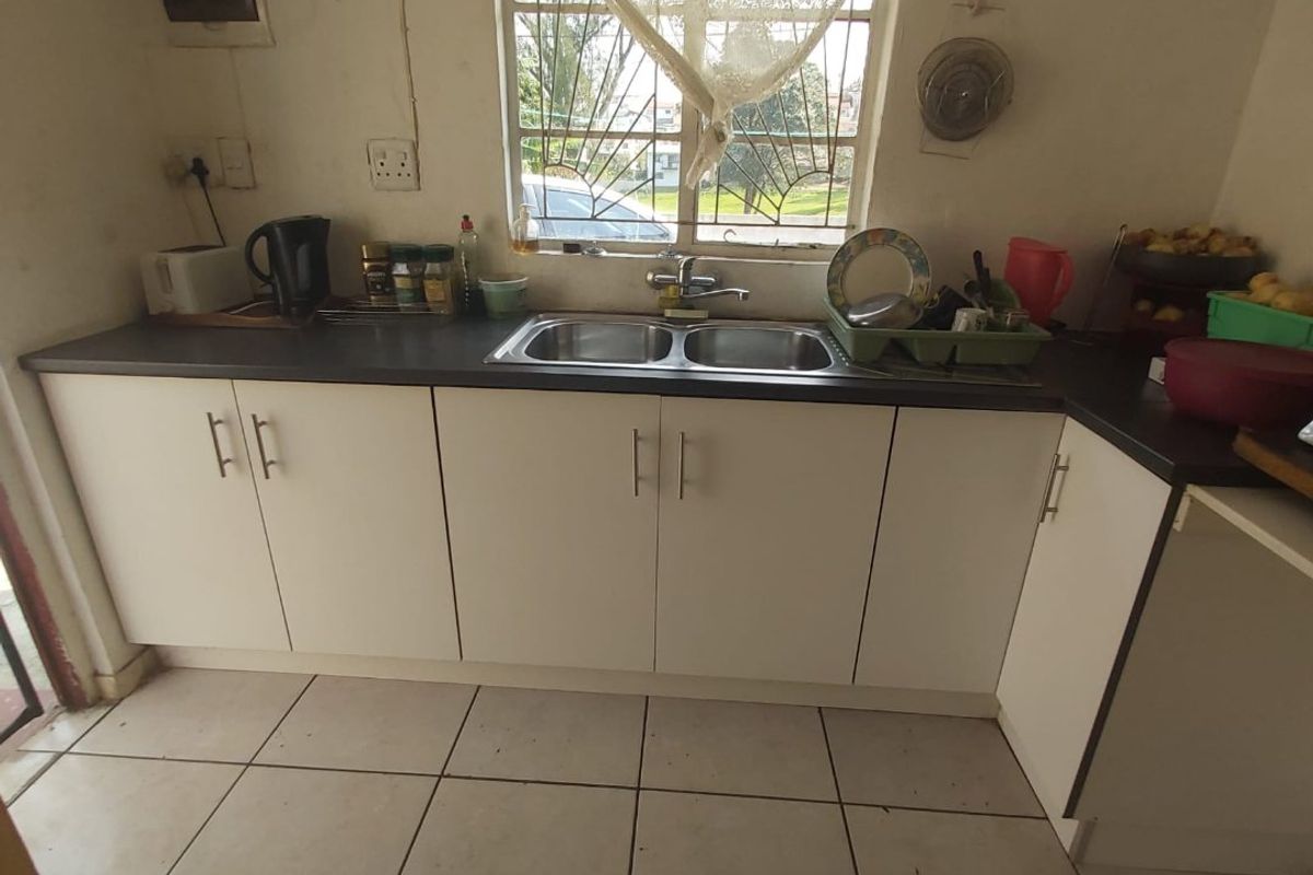 A functional kitchen featuring white cabinetry, dark laminate countertops, a double bowl stainless steel sink, and ceramic tiled flooring.