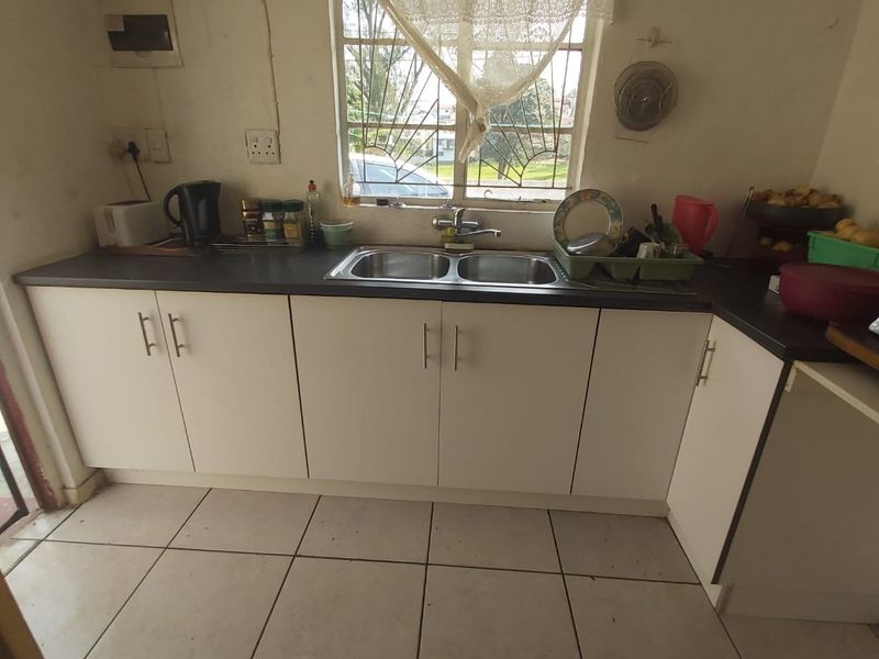 A functional kitchen featuring white cabinetry, dark laminate countertops, a double bowl stainless steel sink, and ceramic tiled flooring.