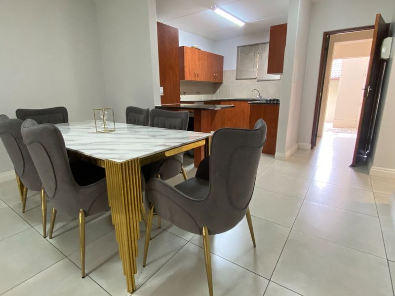 Open plan dining area flowing into a functional kitchen with built-in cabinetry and tiled flooring throughout.
