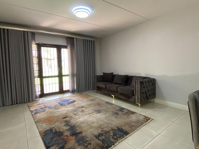 A bright living room featuring large format floor tiles, neutral walls, and a sliding glass door with integrated security gate leading to the exterior.