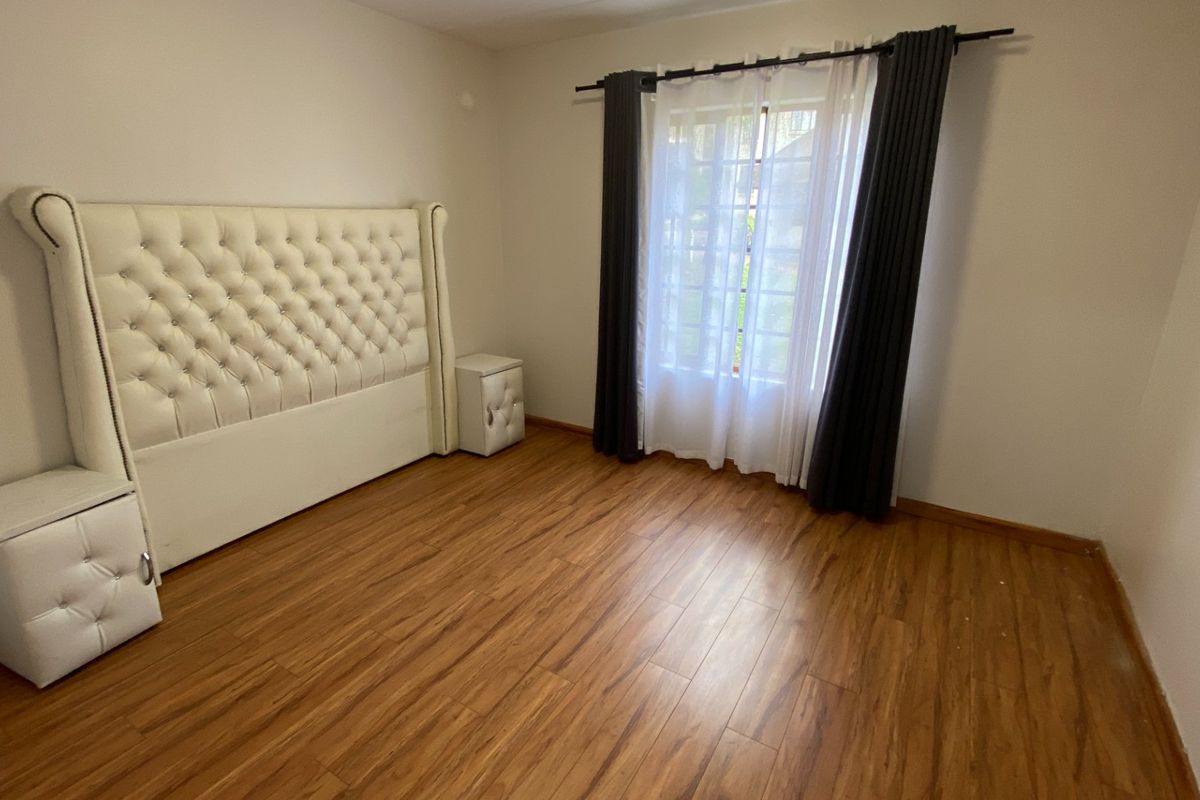 A bedroom featuring warm-toned laminate flooring and a large window with fitted curtain rods.