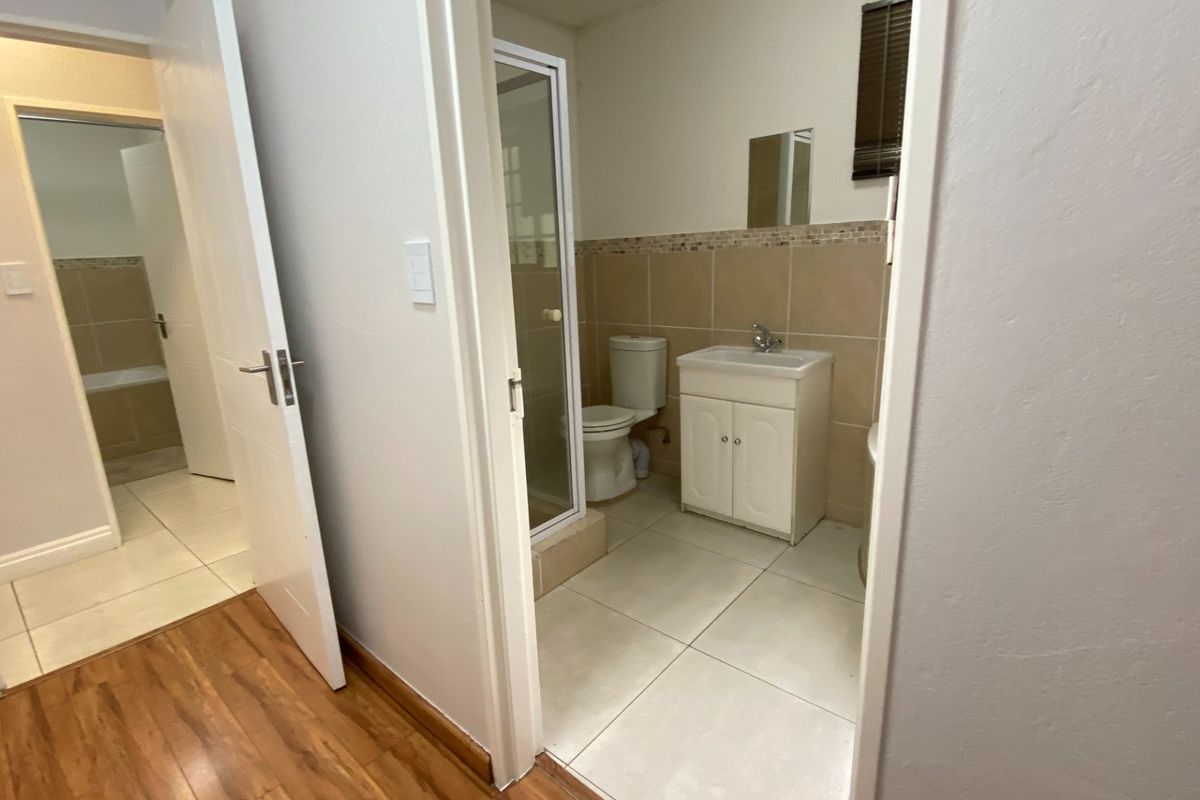 A functional bathroom featuring a vanity cabinet, toilet, and shower enclosure with neutral wall and floor tiling.