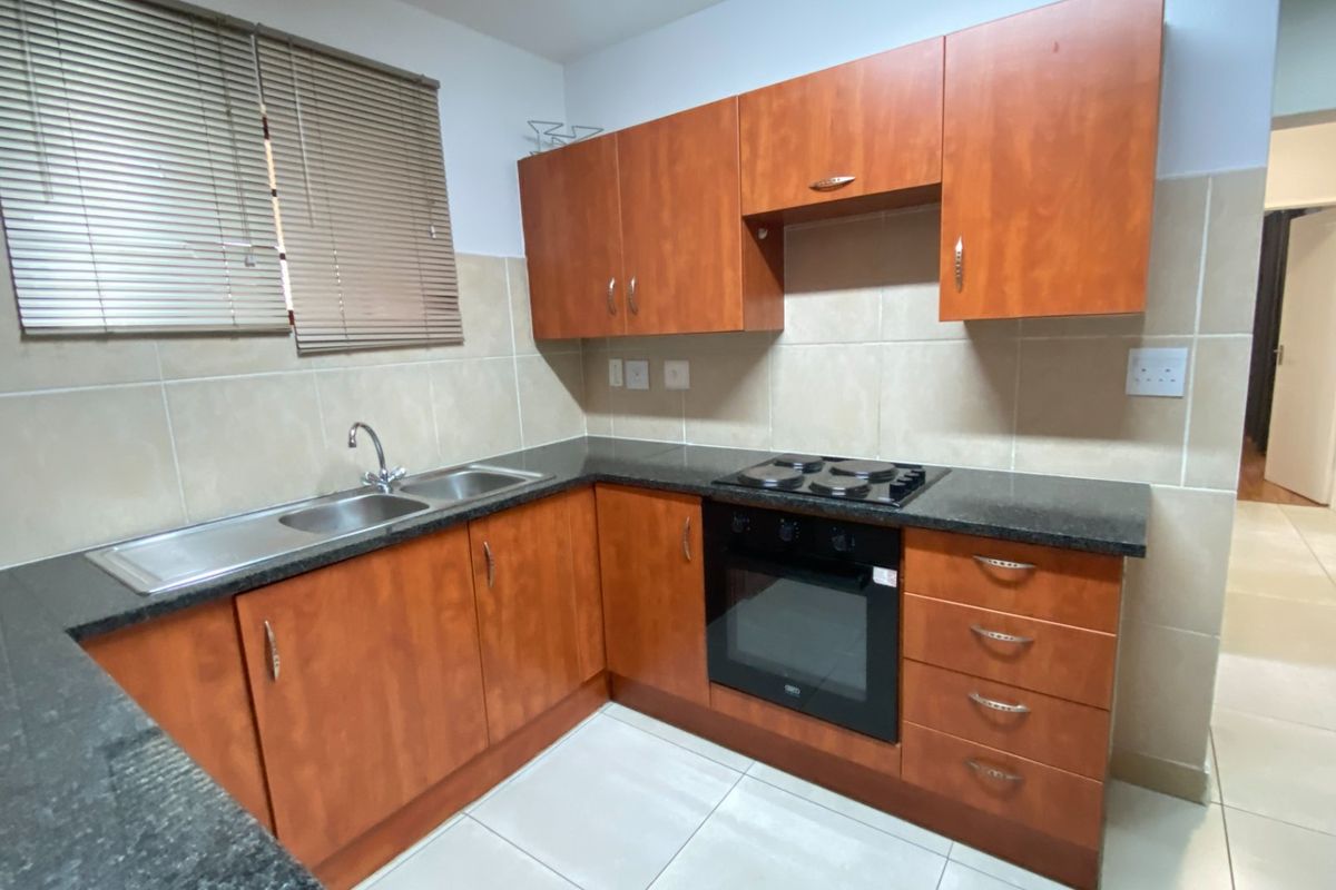 A functional kitchen featuring wooden cabinetry, granite countertops, a built-in oven, electric hob, and tiled finishes throughout.