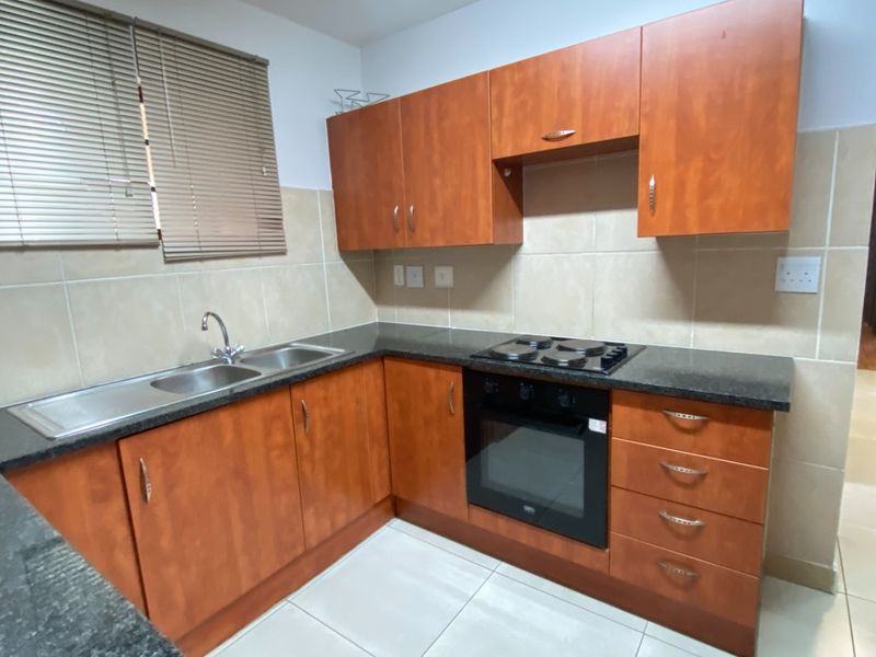 A functional kitchen featuring wooden cabinetry, granite countertops, a built-in oven, electric hob, and tiled finishes throughout.