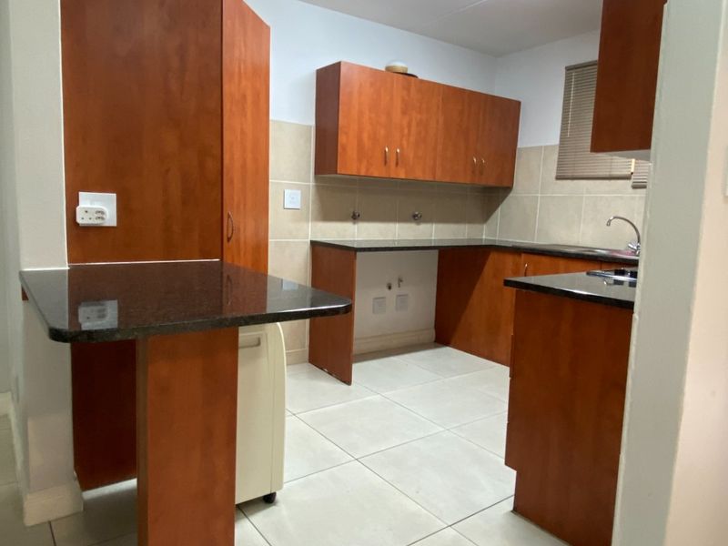 A functional kitchen featuring wooden cabinetry, granite countertops, tiled backsplash, and tiled flooring, offering a clean and practical workspace.